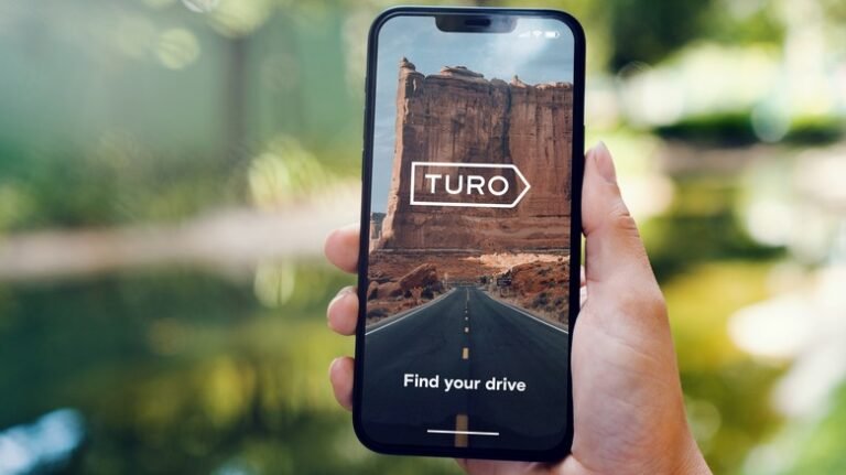 A person holding a phone displaying the Turo car sharing app.